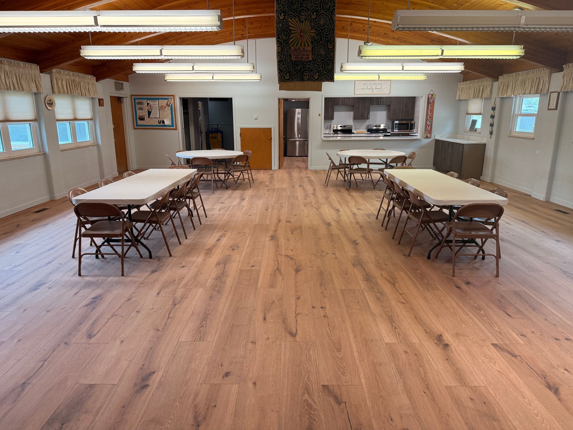 Empty community hall with folding tables, chairs, wood floor, and fluorescent ceiling lights