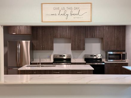 Modern kitchen with stainless appliances, dark wood cabinets, white island, and framed wall sign