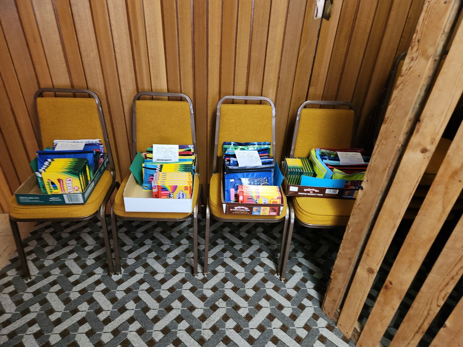 Four yellow chairs lined up against a wood-paneled wall, each holding books and toy boxes.
