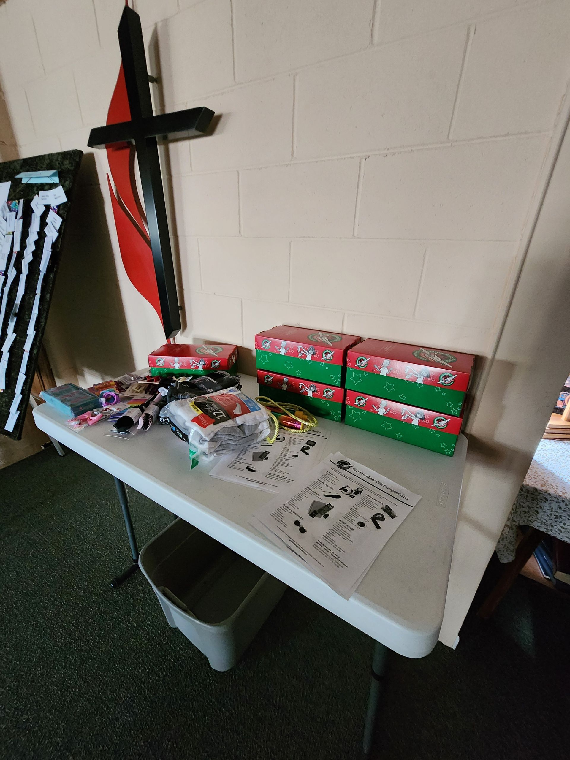 Table with stacks of red-and-green packages, snacks, and small items against a white wall