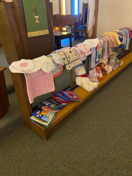 Children’s books and stuffed toys displayed on a church pew with knitted items draped over the back