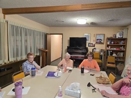 People seated around a table in a library, with a TV and bookshelf in the background