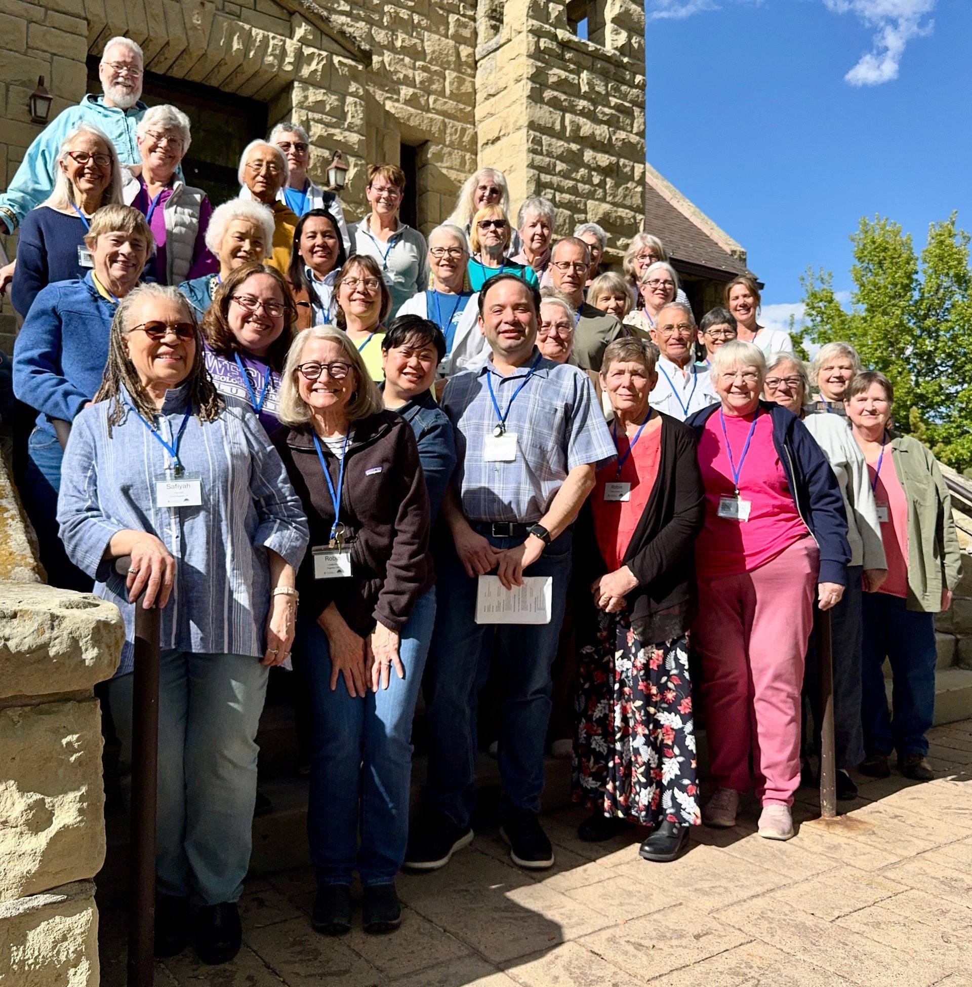 Group of smiling people posing on stone steps outside a historic building in bright sunlight