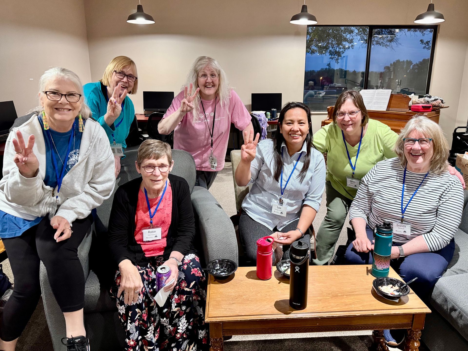 Group of smiling people posing in a lounge with couches, coffee table, and laptop desks behind them.
