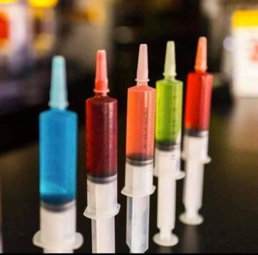 Five syringes filled with colorful liquids, including blue, red, orange, green, and red, arranged in a row.