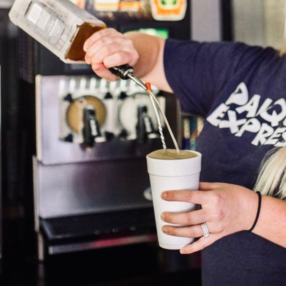 Person pouring a drink from a bottle into a white cup, in front of a slushy machine.
