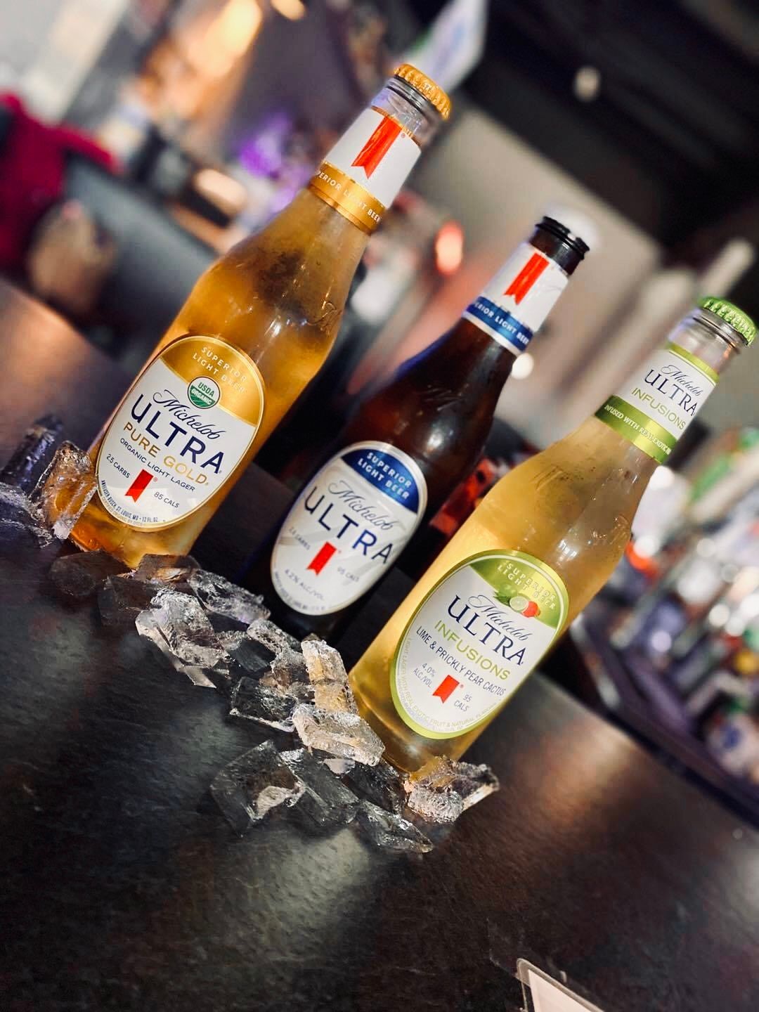 Three Michelob Ultra beers in ice on a bar; labels are gold, blue, and green.