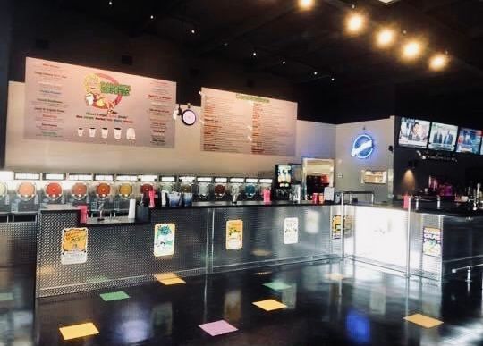 Interior of a slushy bar with colorful frozen drink dispensers and menu boards; metal counters.