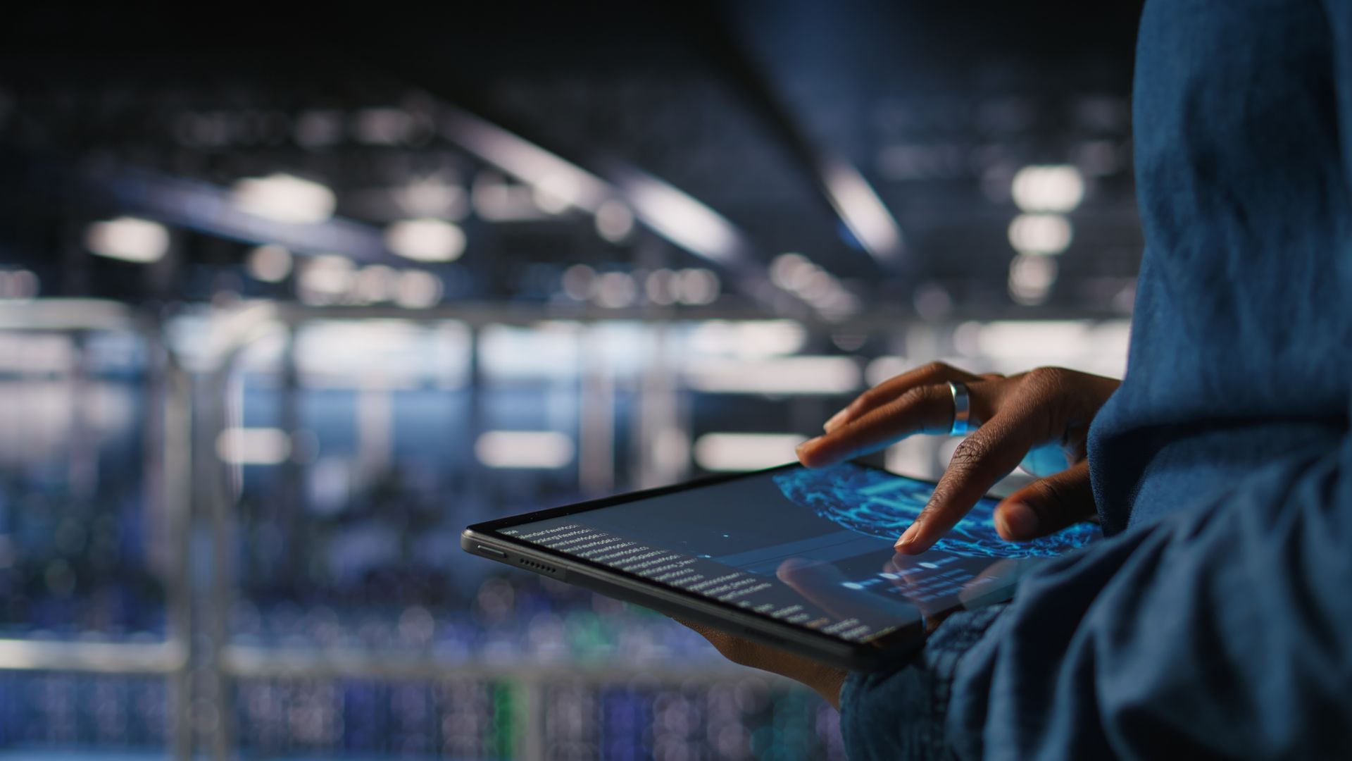 Person using a tablet in a dimly lit office or server room with blurred lights in the background