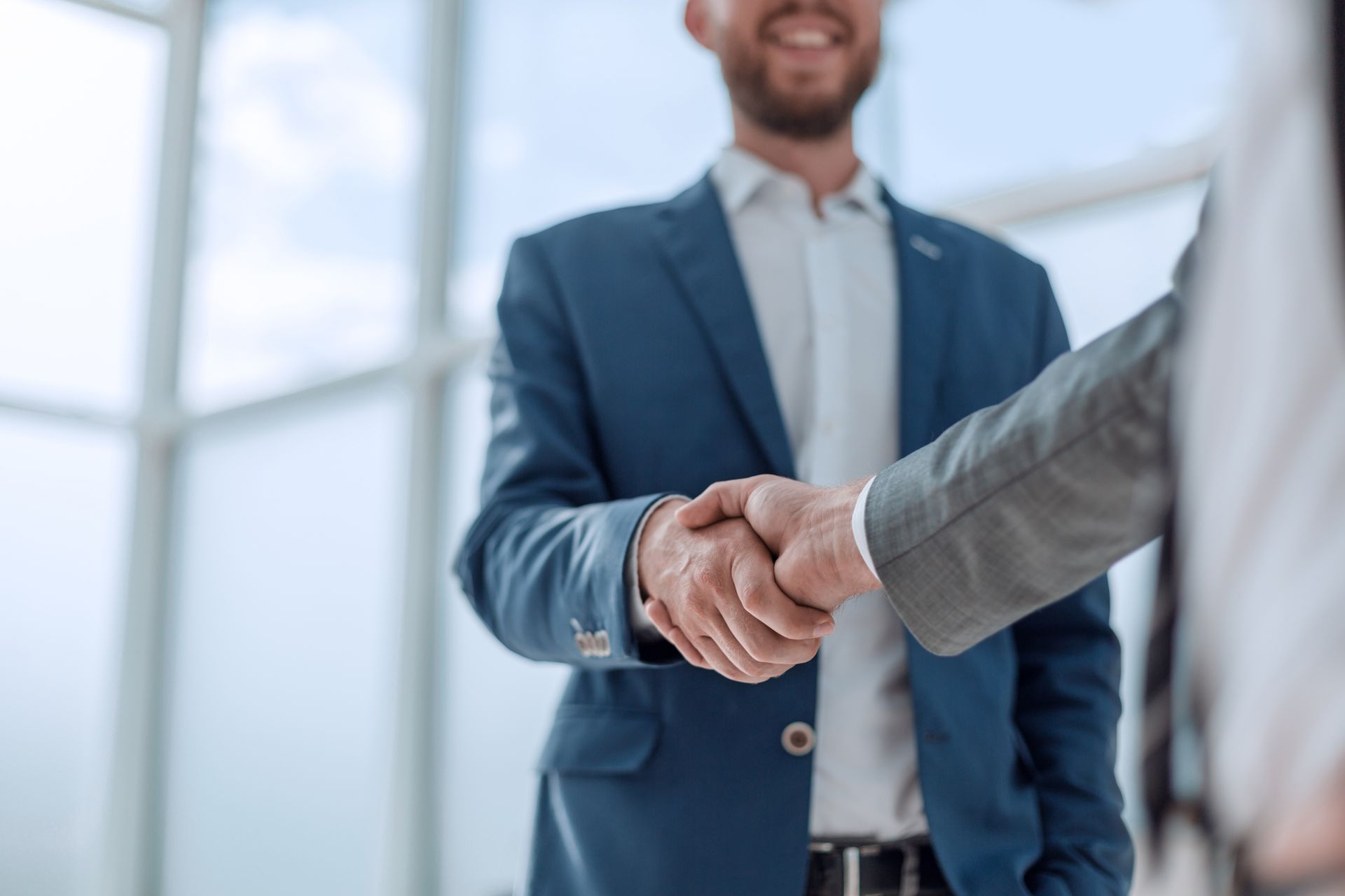 Two professionals shaking hands in a bright office lobby, one in a blue suit