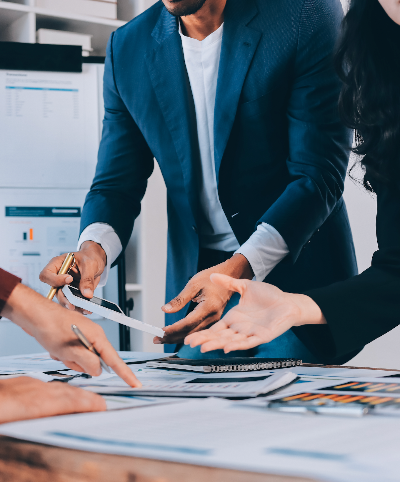 Colleagues in suits point and collaborate over charts at a desk in an office.