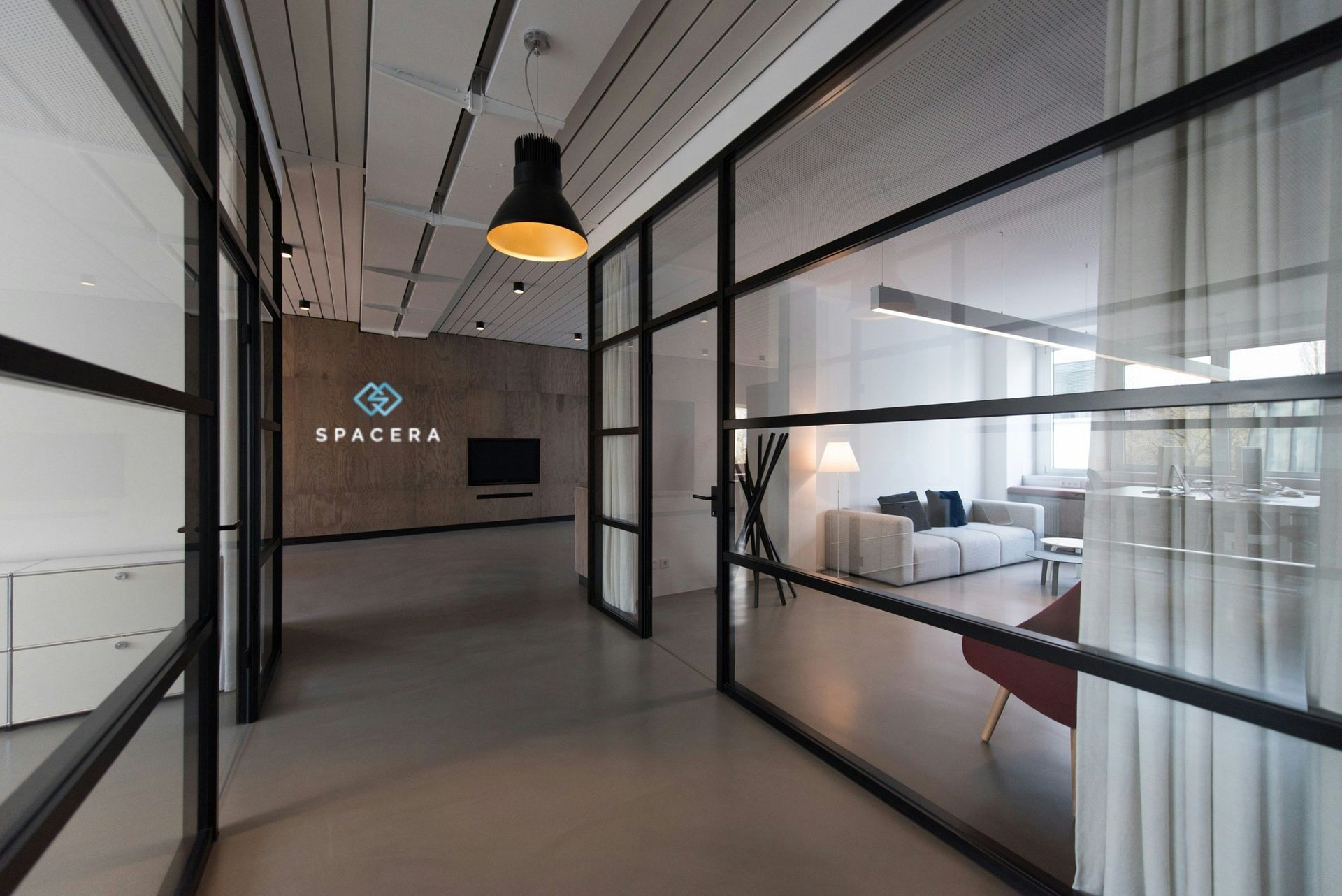 Modern office hallway with glass-walled meeting rooms and a hanging pendant light