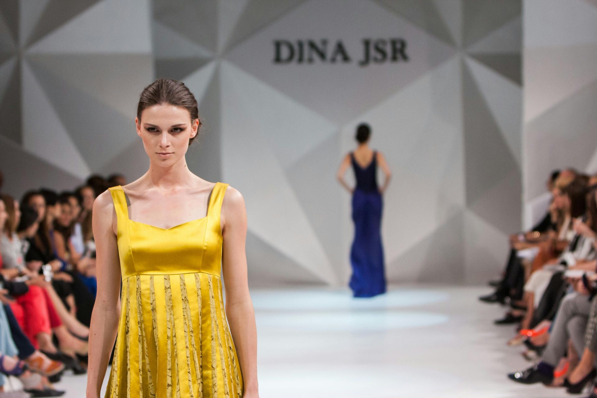 Una donna con un vestito giallo sta sfilando sulla passerella di una sfilata di moda
