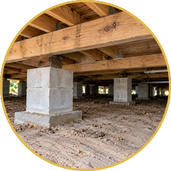 Crawl space under a house with wooden beams and concrete support piers on dirt soil