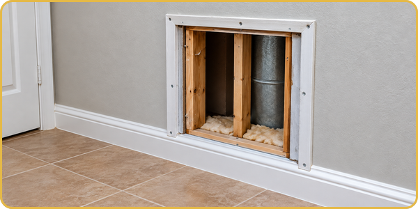 Open wall access panel with exposed framing beside tiled floor and white baseboard