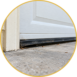 Close-up of a white garage door with a black damaged bottom seal on a concrete driveway