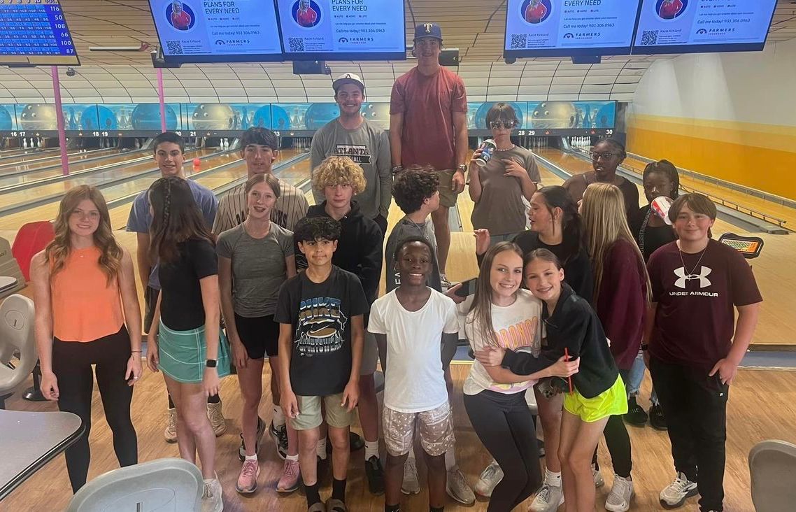 A group of young people are posing for a picture in a bowling alley.