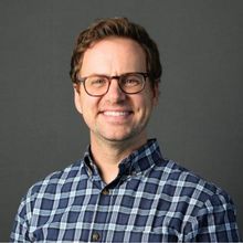 A man wearing glasses and a plaid shirt is smiling for the camera.