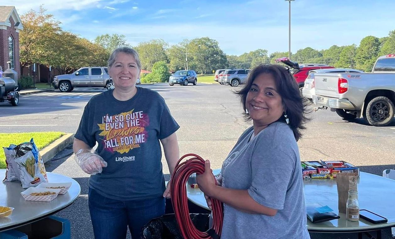 Two women are standing next to each other in a parking lot holding a rope.