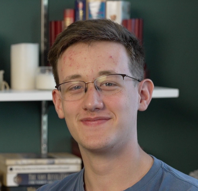 A young man wearing glasses is smiling for the camera