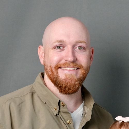 A bald man with a beard is smiling while holding a little girl.