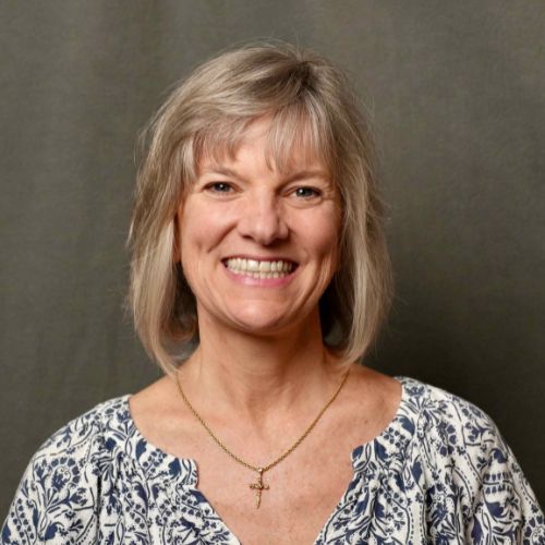 A woman wearing a cross necklace is smiling for the camera.
