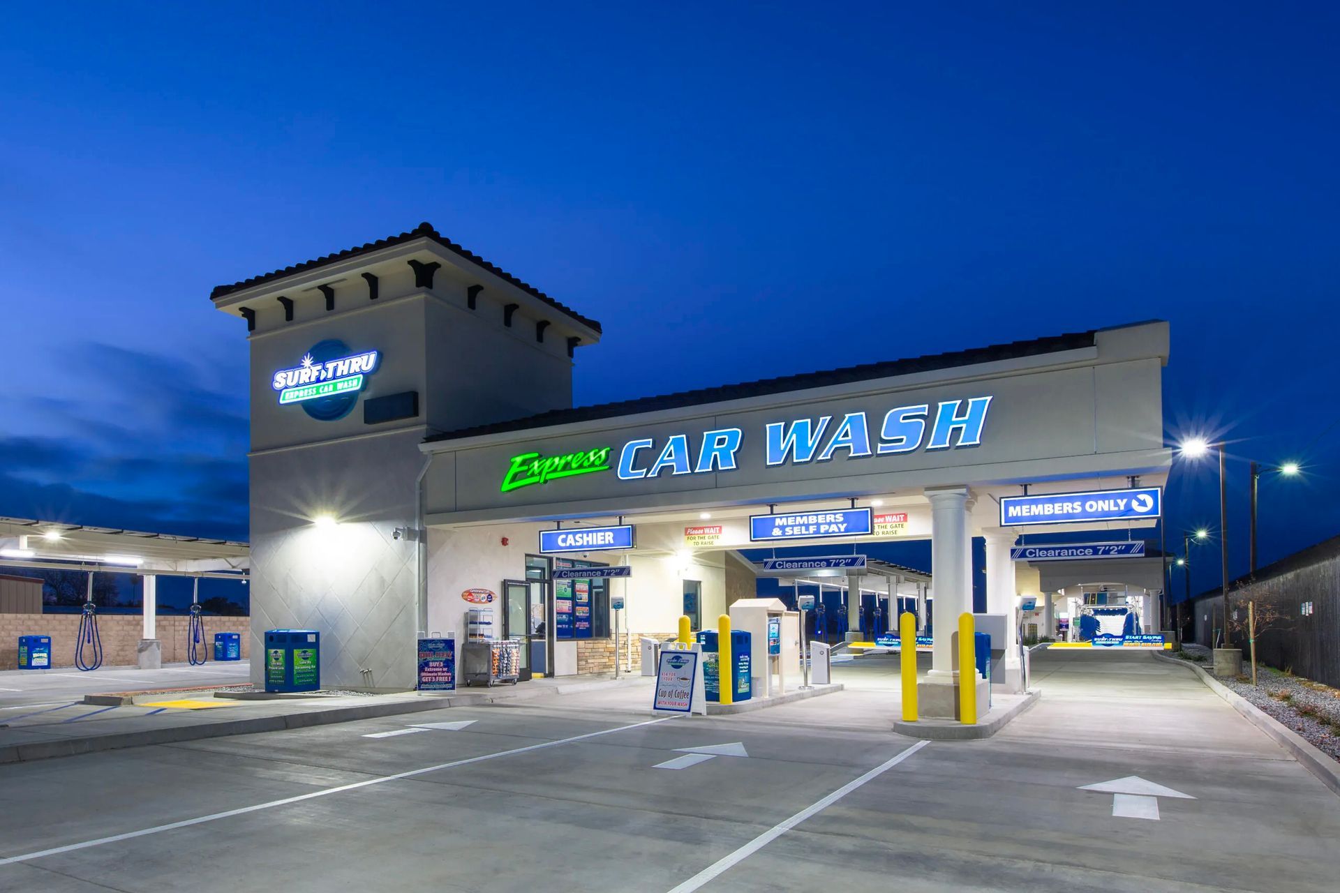 A car wash is lit up at night with a parking lot in front of it.