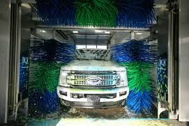 A truck is going through a car wash with blue and green brushes.