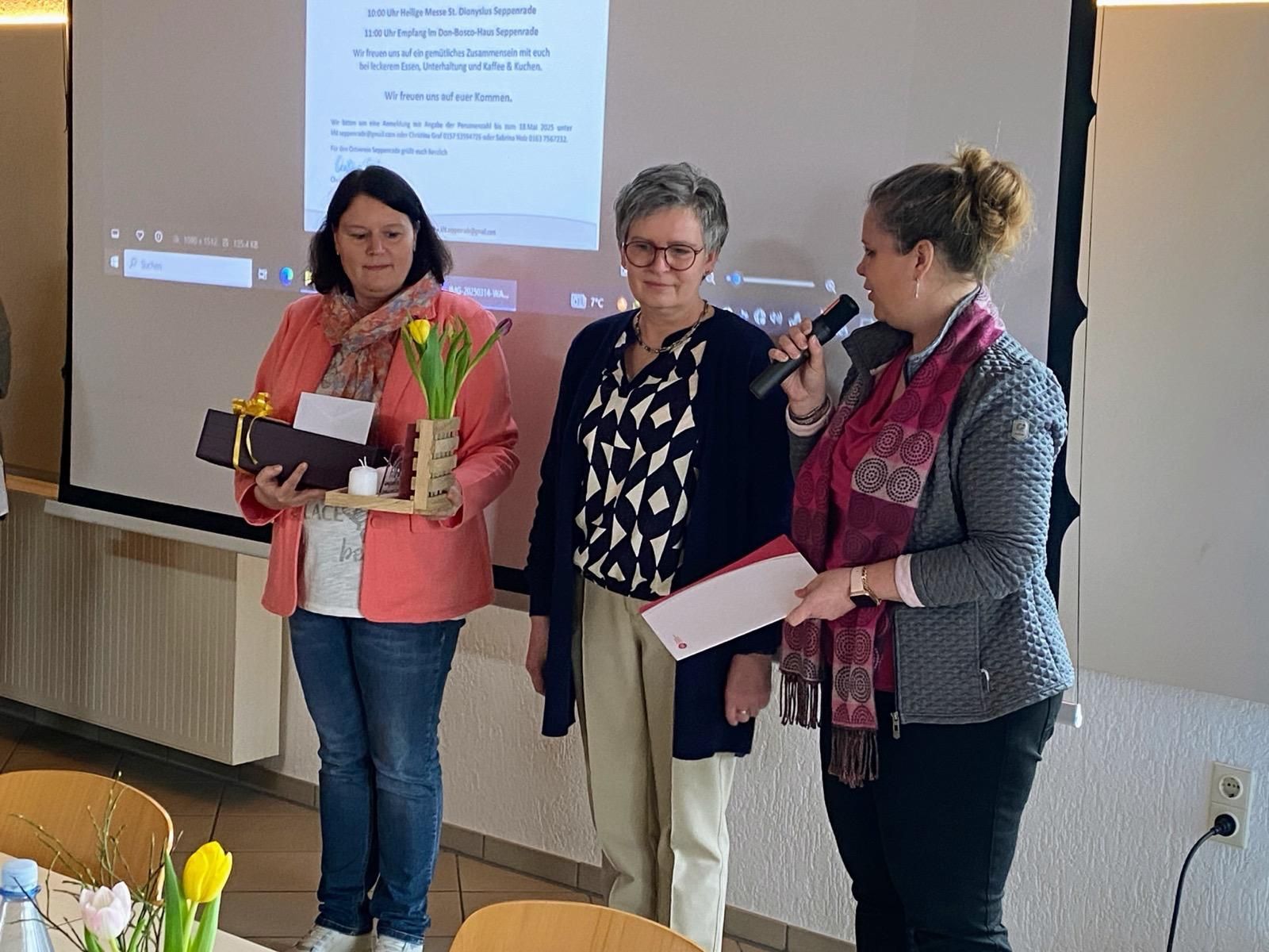 Drei Frauen stehen vor einer Projektionsleinwand.