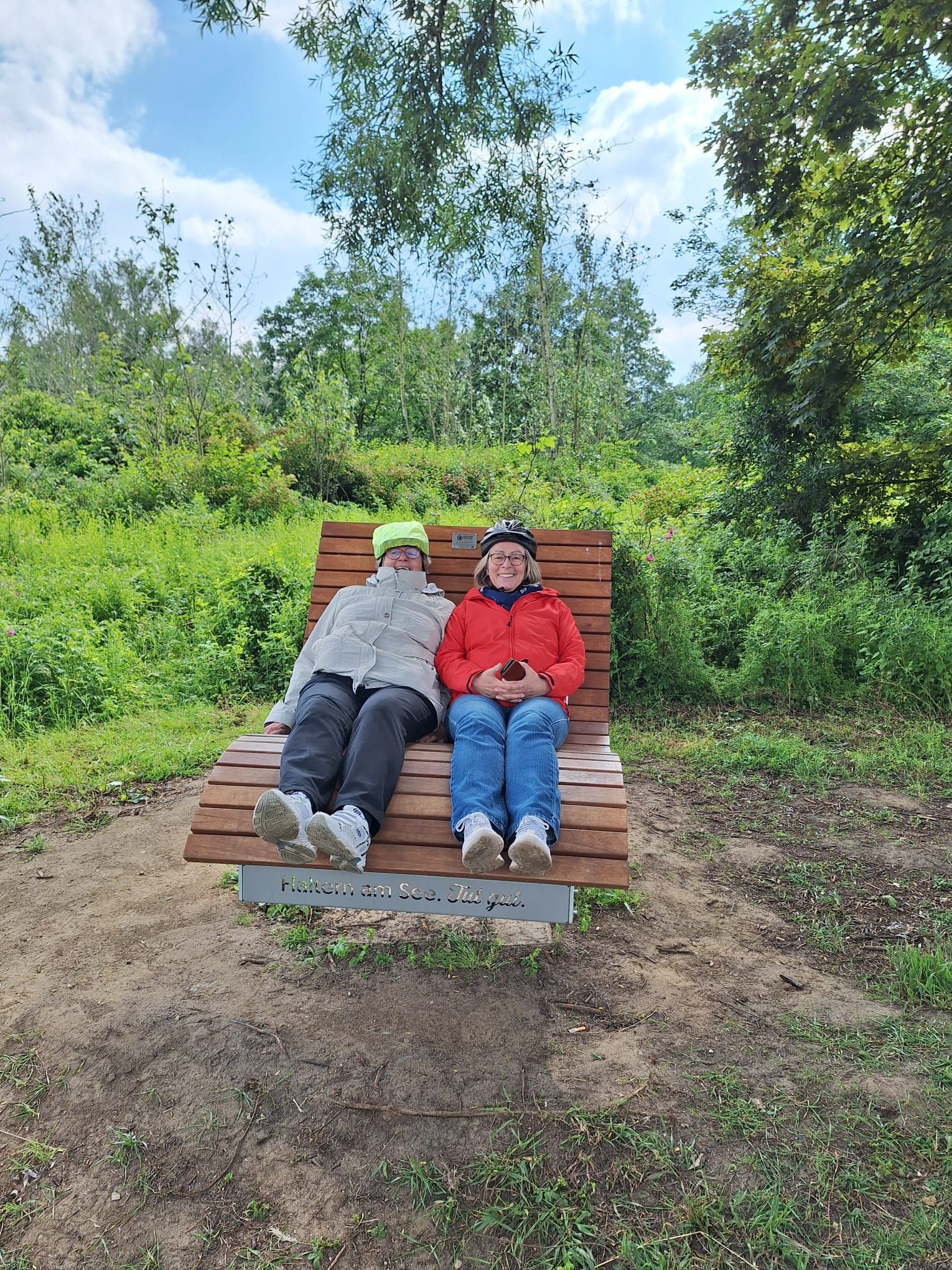 Zwei Personen sitzen auf einer Holzbank im Gras.