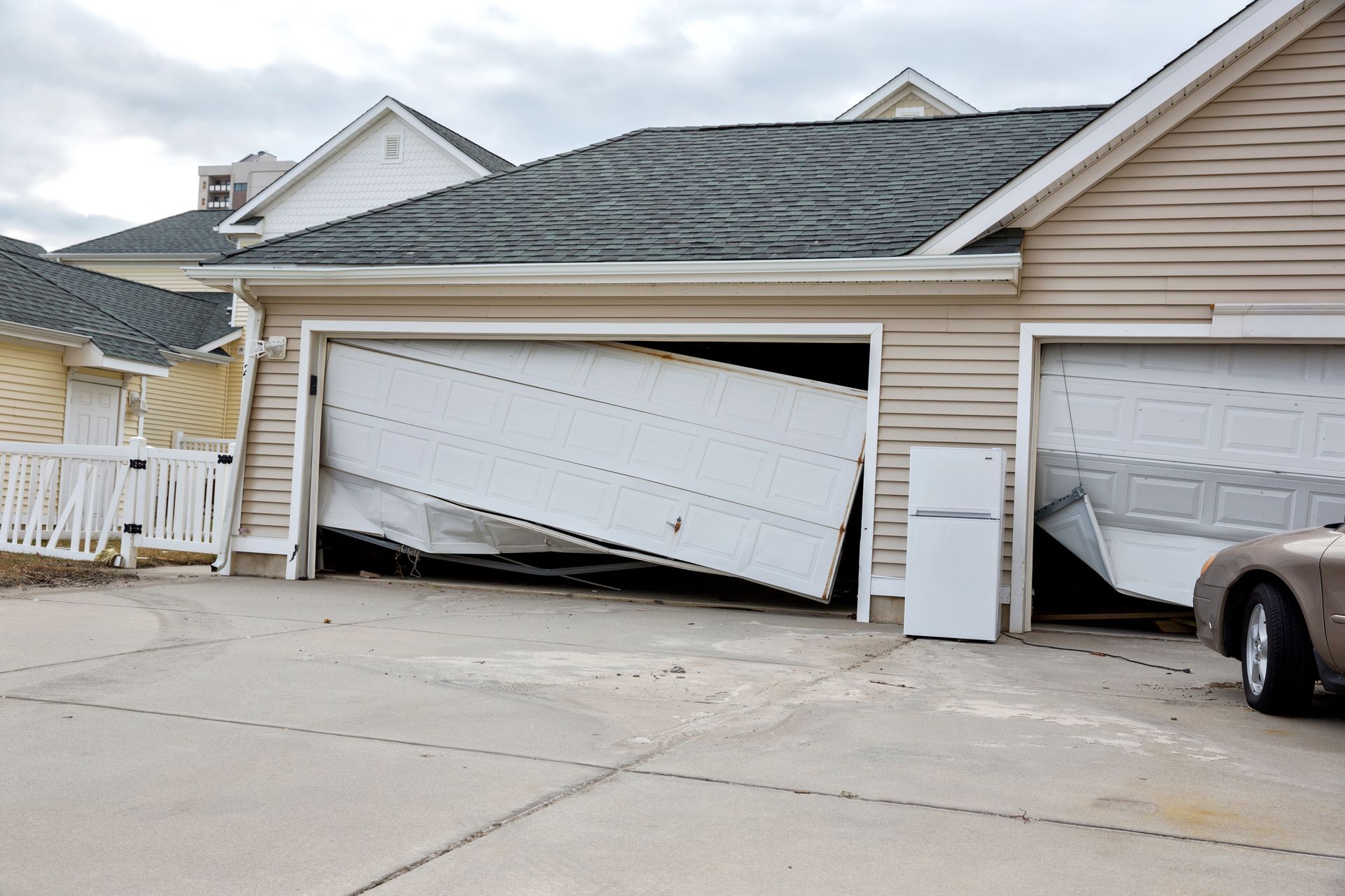 Damaged garage door, leaning inwards, exposing interior. Another garage door damaged next to it.