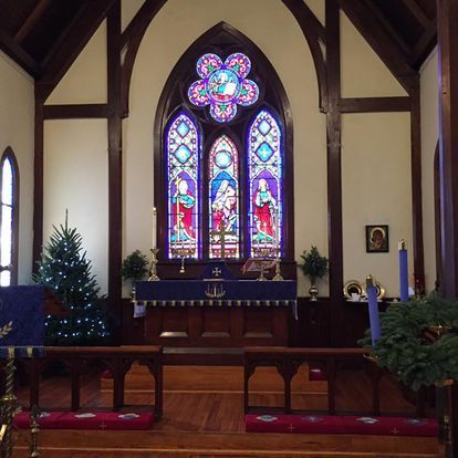 Interior of a church with a colorful stained-glass window above the altar, a Christmas tree, and wooden pews.