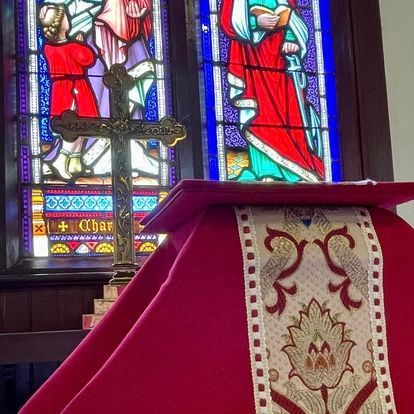 Cross on red-draped altar with stained-glass windows in background.