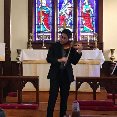 Jonathan Kuo playing a violin in a church, stained glass window backdrop.