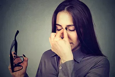 Lady holding a pair of frames while rubbing eyes
