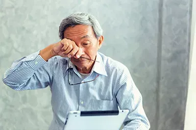 Man rubbing his eye swhile reading from a tablet