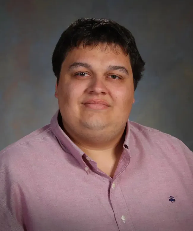 Portrait of a smiling person in a pink button-up shirt against a gray studio background