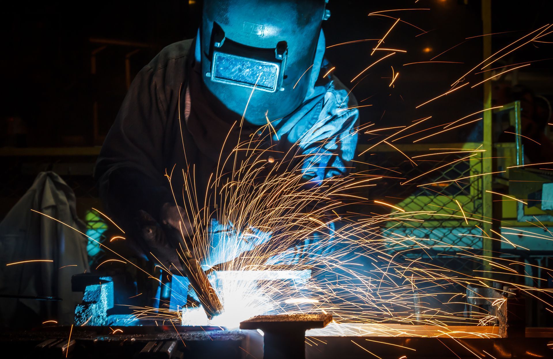 Welder in protective helmet and gloves welding steel amid bright sparks.