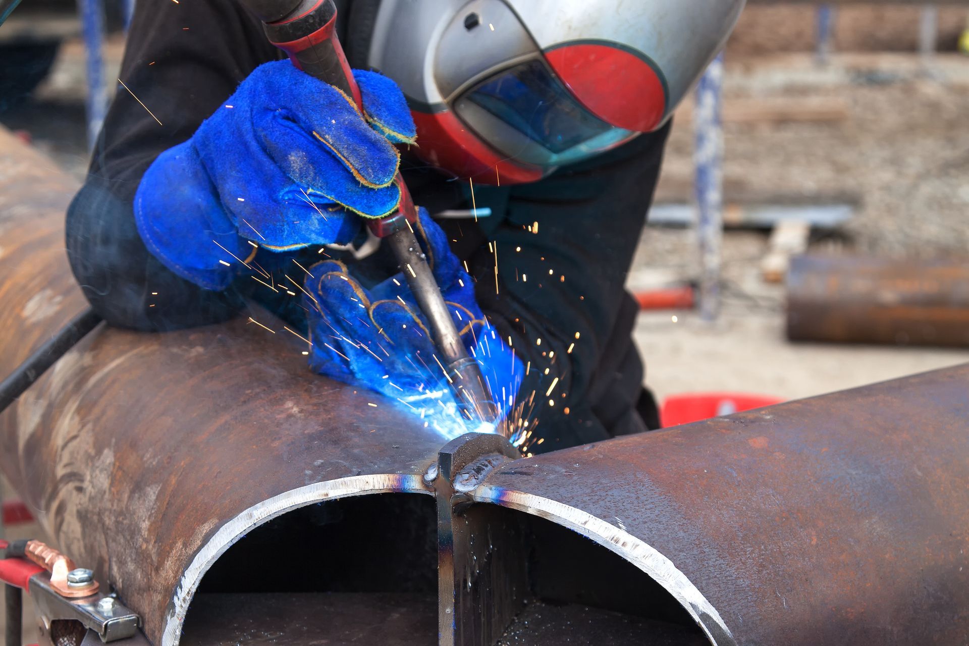 Welder in blue gloves welding a large steel pipe joint.