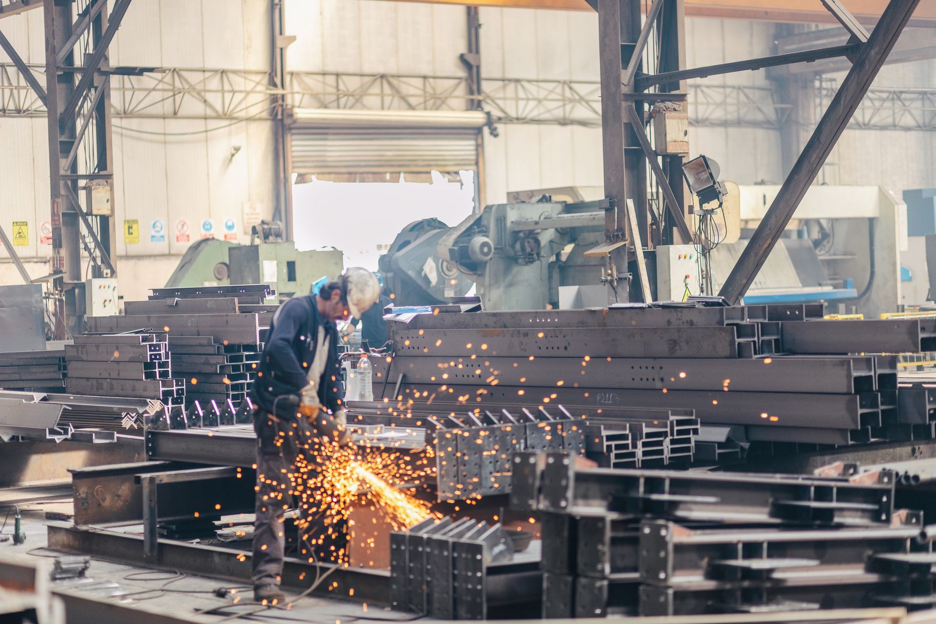 : A steel fabricator in a factory creates sparks while working on a piece of steel stock.