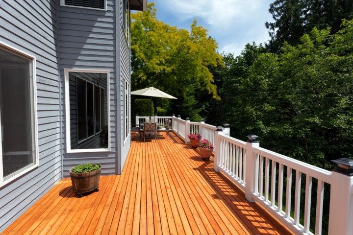 A wooden deck with a white railing extends from a gray house, featuring potted plants and an umbrella-covered dining area.