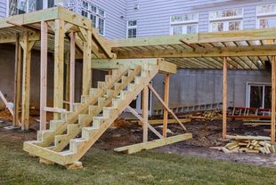 A wooden deck under construction with a staircase frame attached to the house exterior.