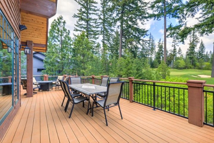 A wooden deck with patio furniture overlooks a green, forested landscape under a cloudy blue sky.