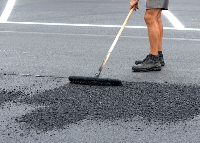 Worker spreading black asphalt on a road with a rake during pavement repair