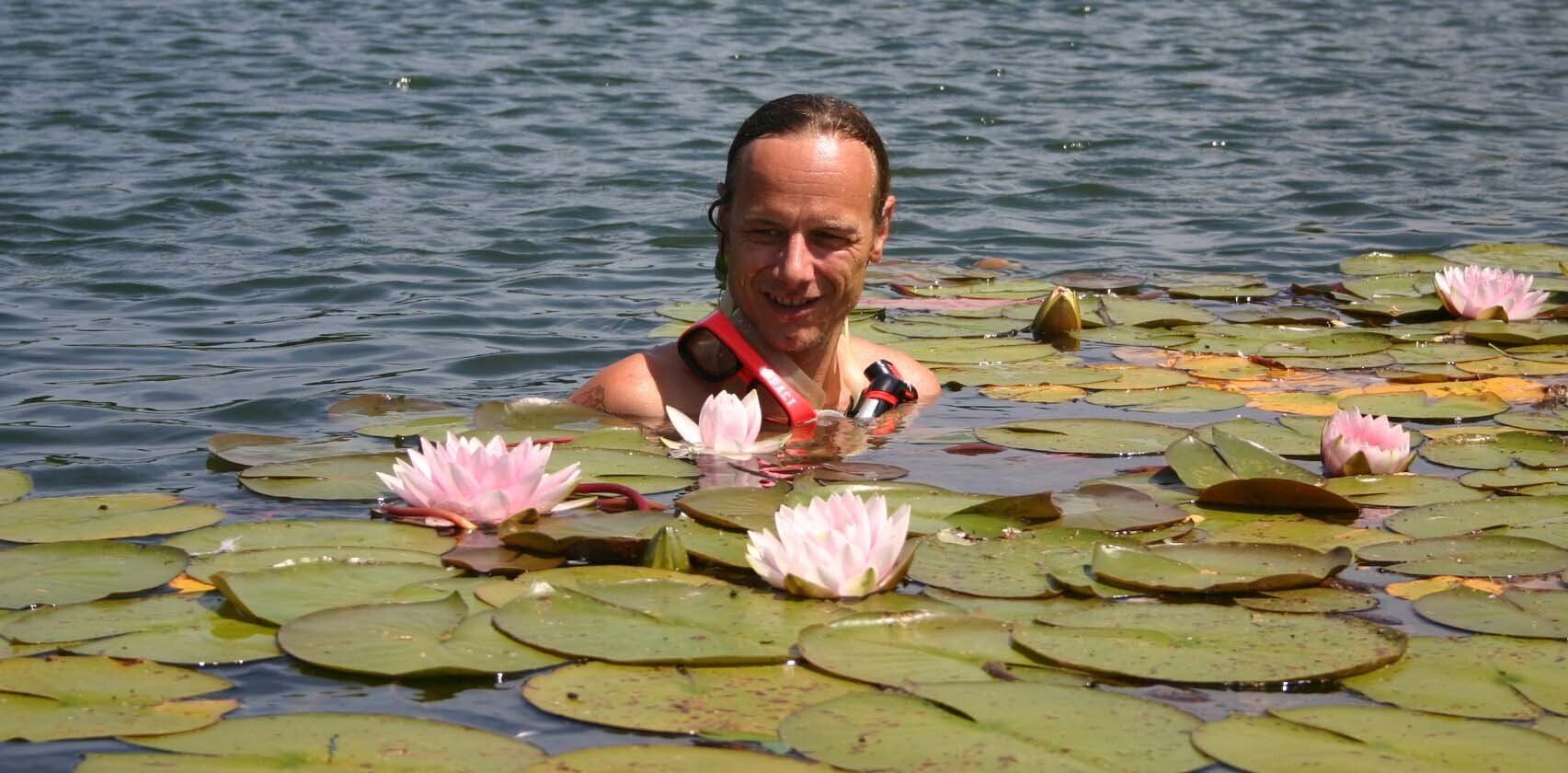 A man is swimming in a lake surrounded by water lilies.