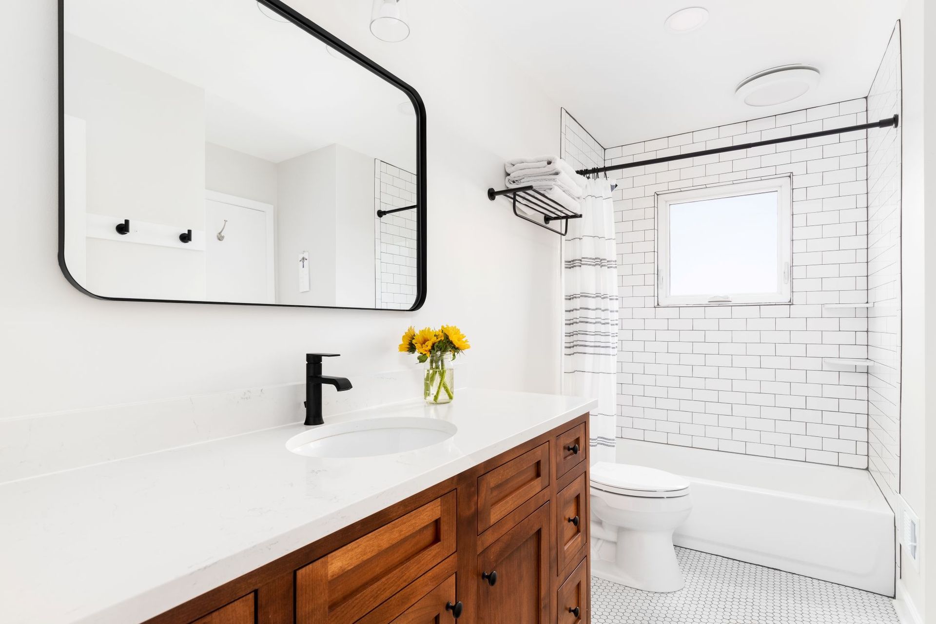 Bright white bathroom with black fixtures, wooden vanity, and a tub-shower with subway tile.