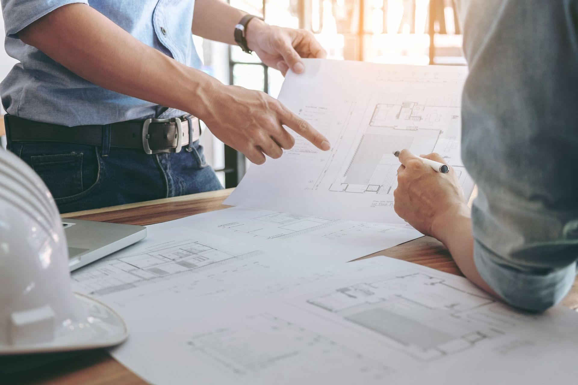 Two people reviewing blueprints on a table, with a hard hat nearby in an office setting