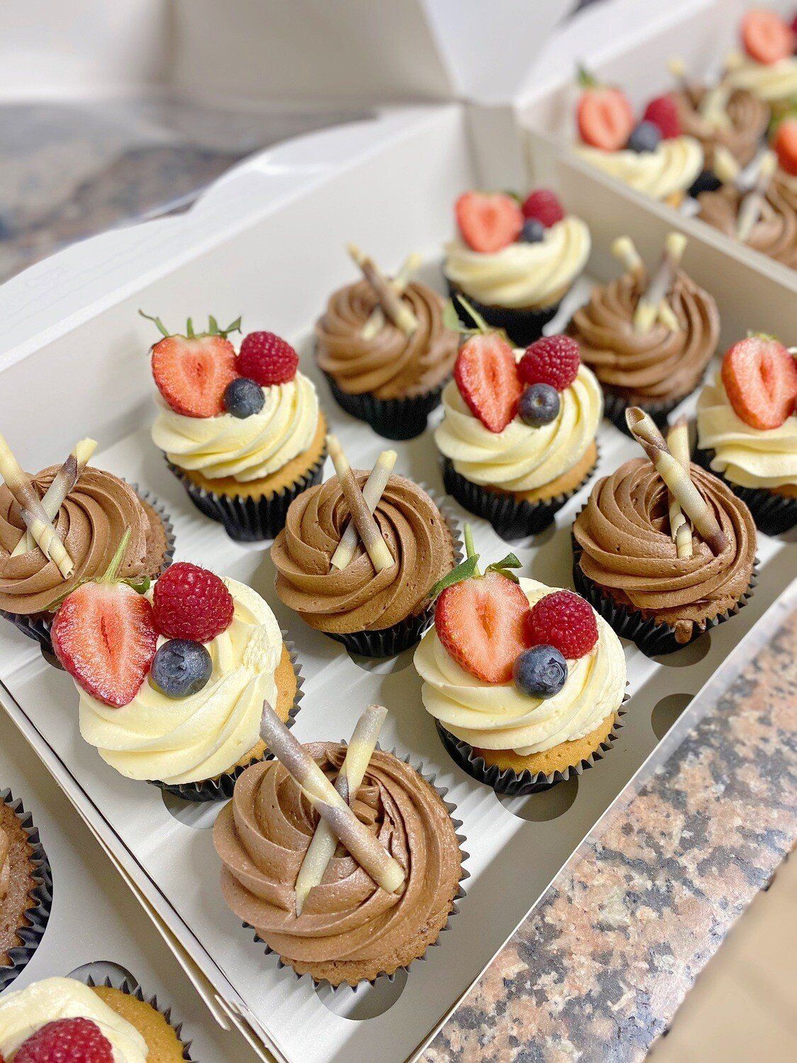 A box of cupcakes with chocolate frosting and berries on top.