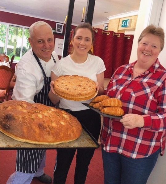 Gabriella and family holding trays of food including a pie and croissants