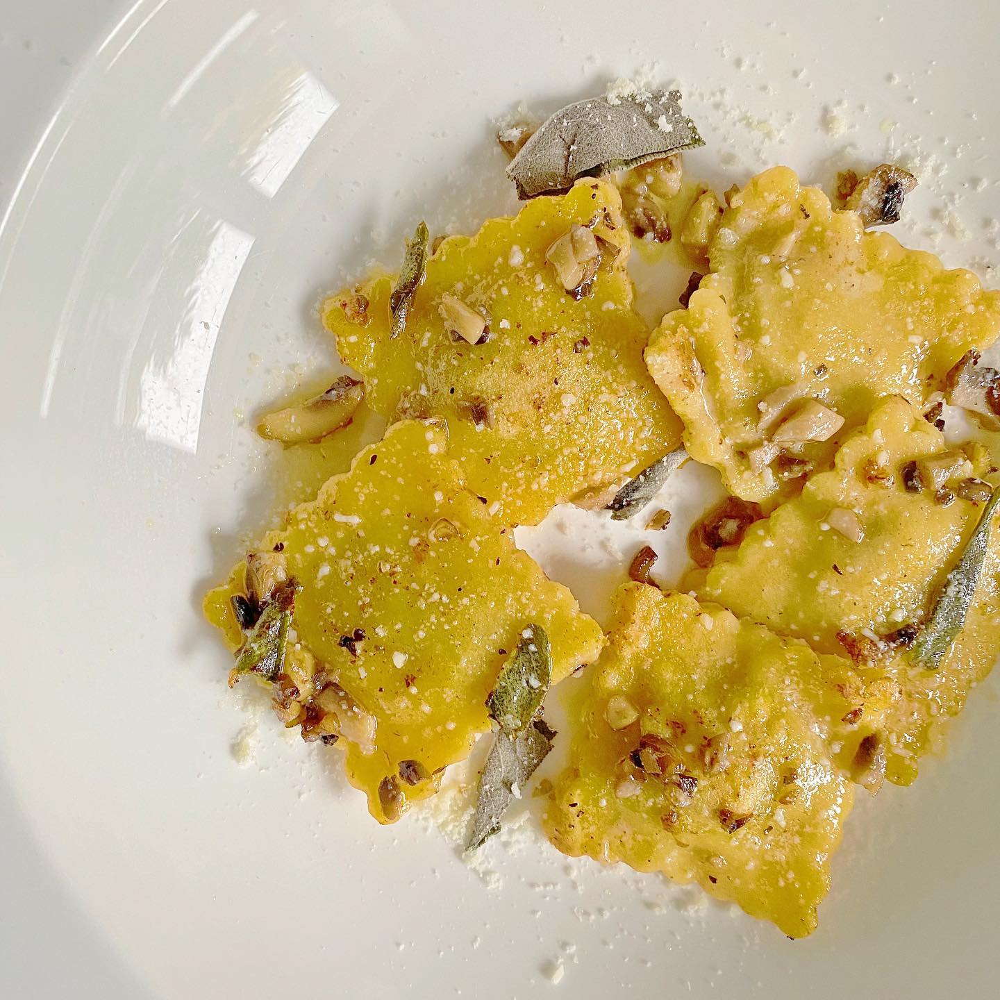 A close up of a white plate topped with ravioli and cheese.